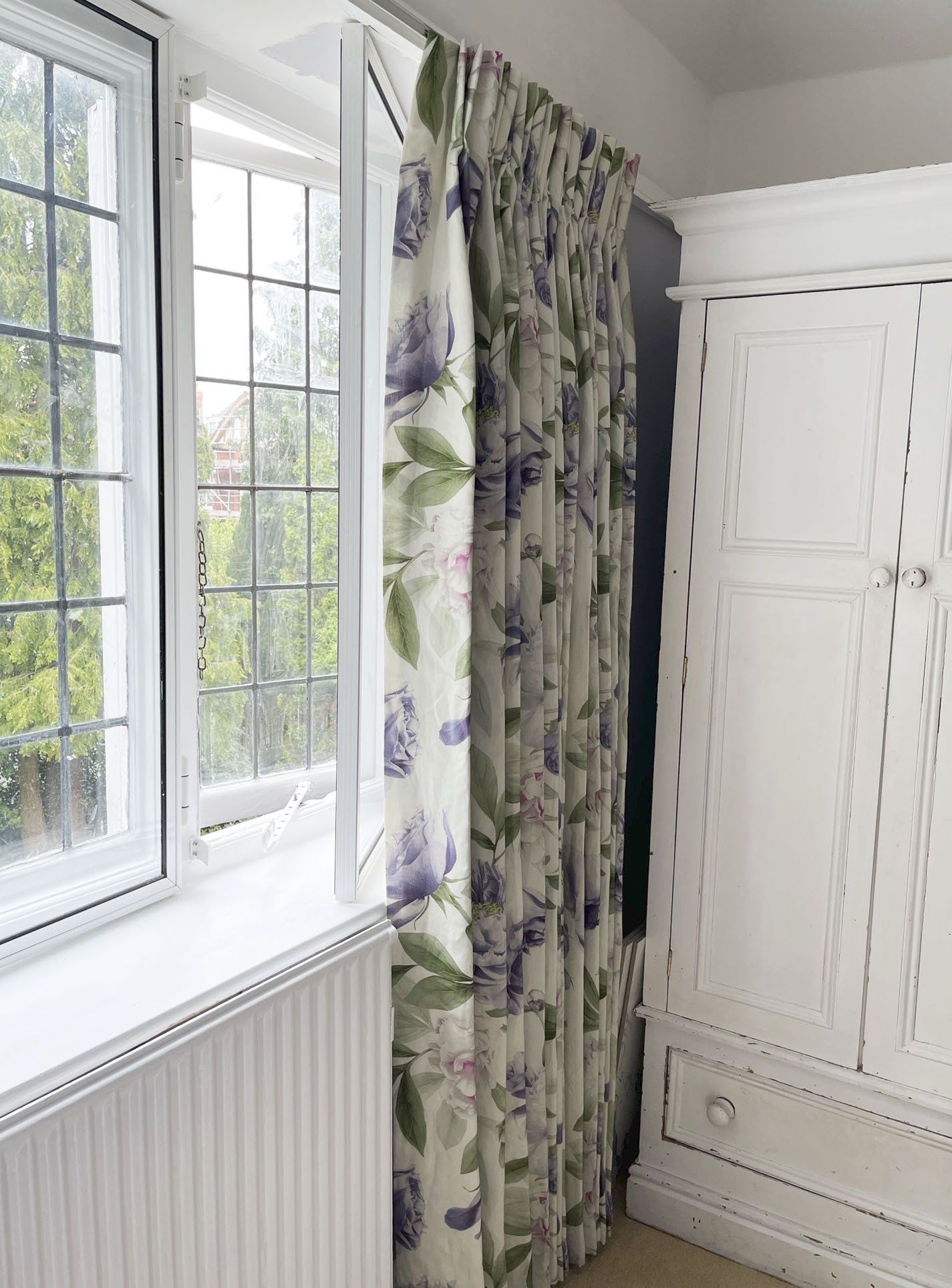 A bedroom with a window , dresser , and curtains.
