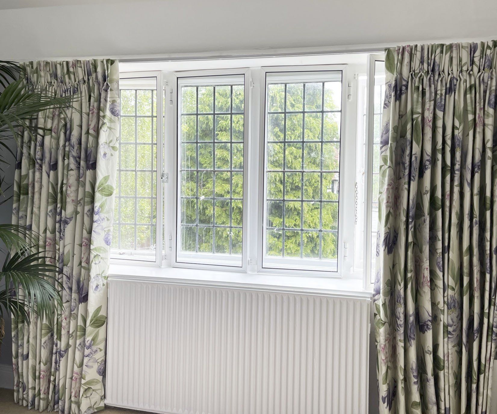 A living room with a large window and floral curtains.