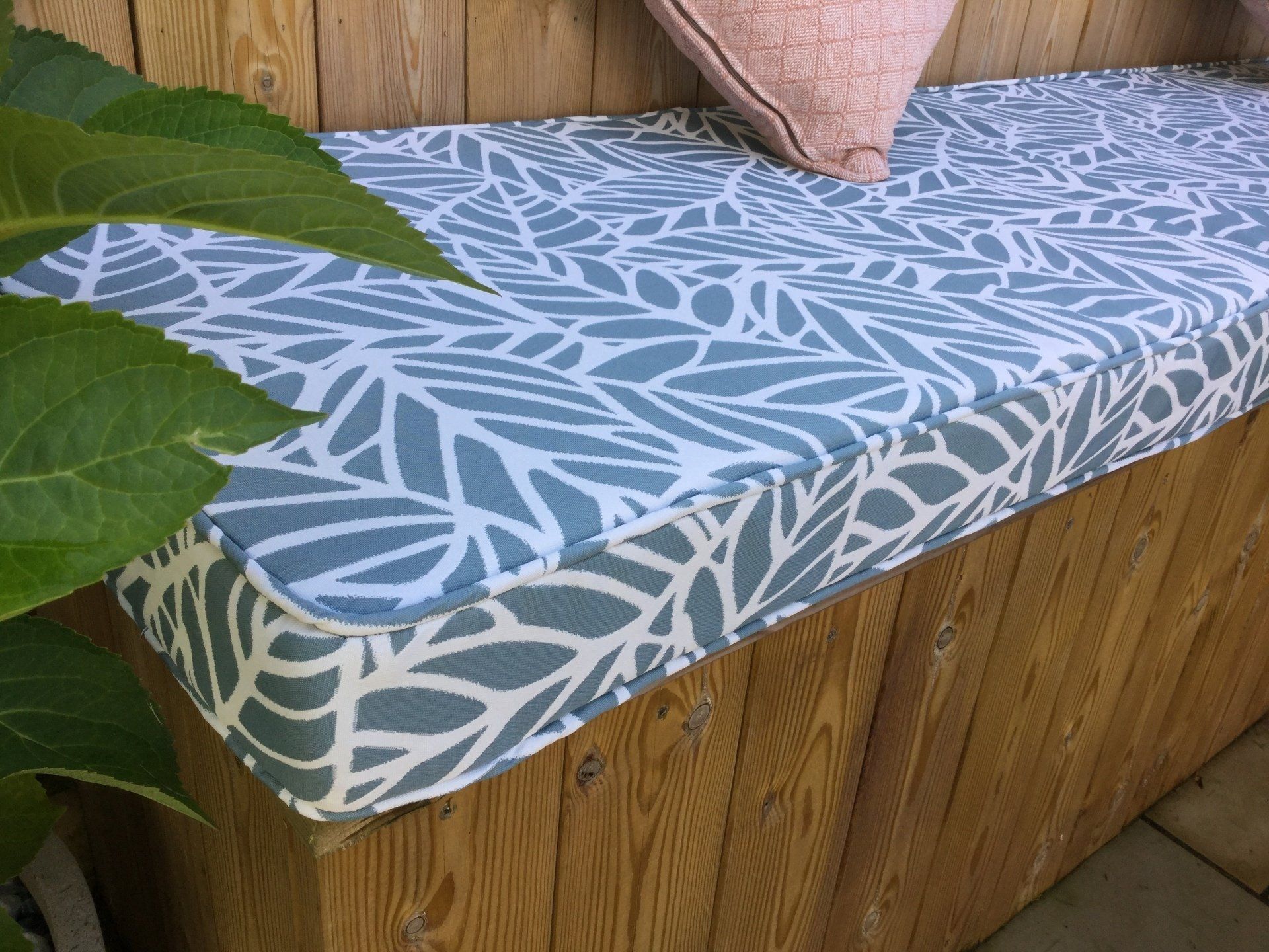 A wooden bench with a cushion and pillows on it.