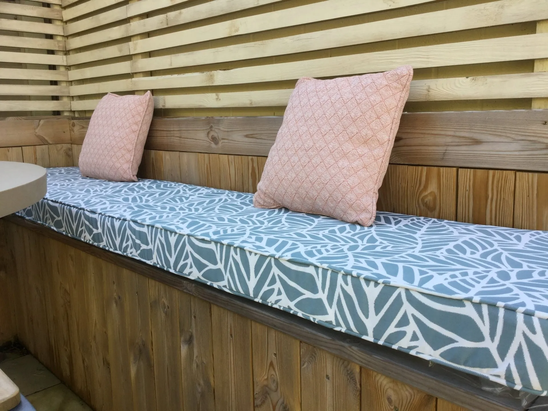 A wooden bench with a cushion and two pillows on it.