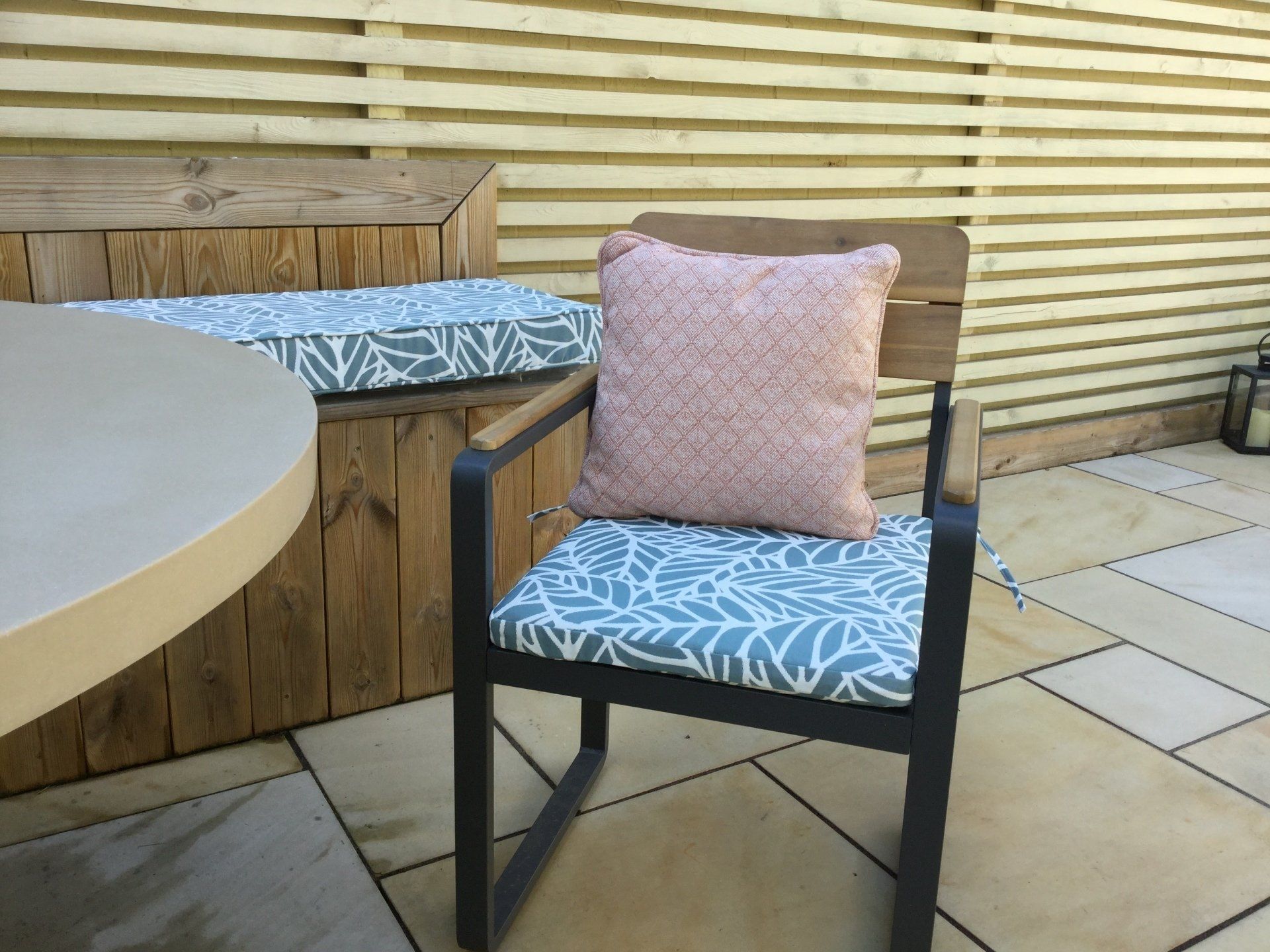 A chair with a pillow on it is sitting on a patio next to a table.