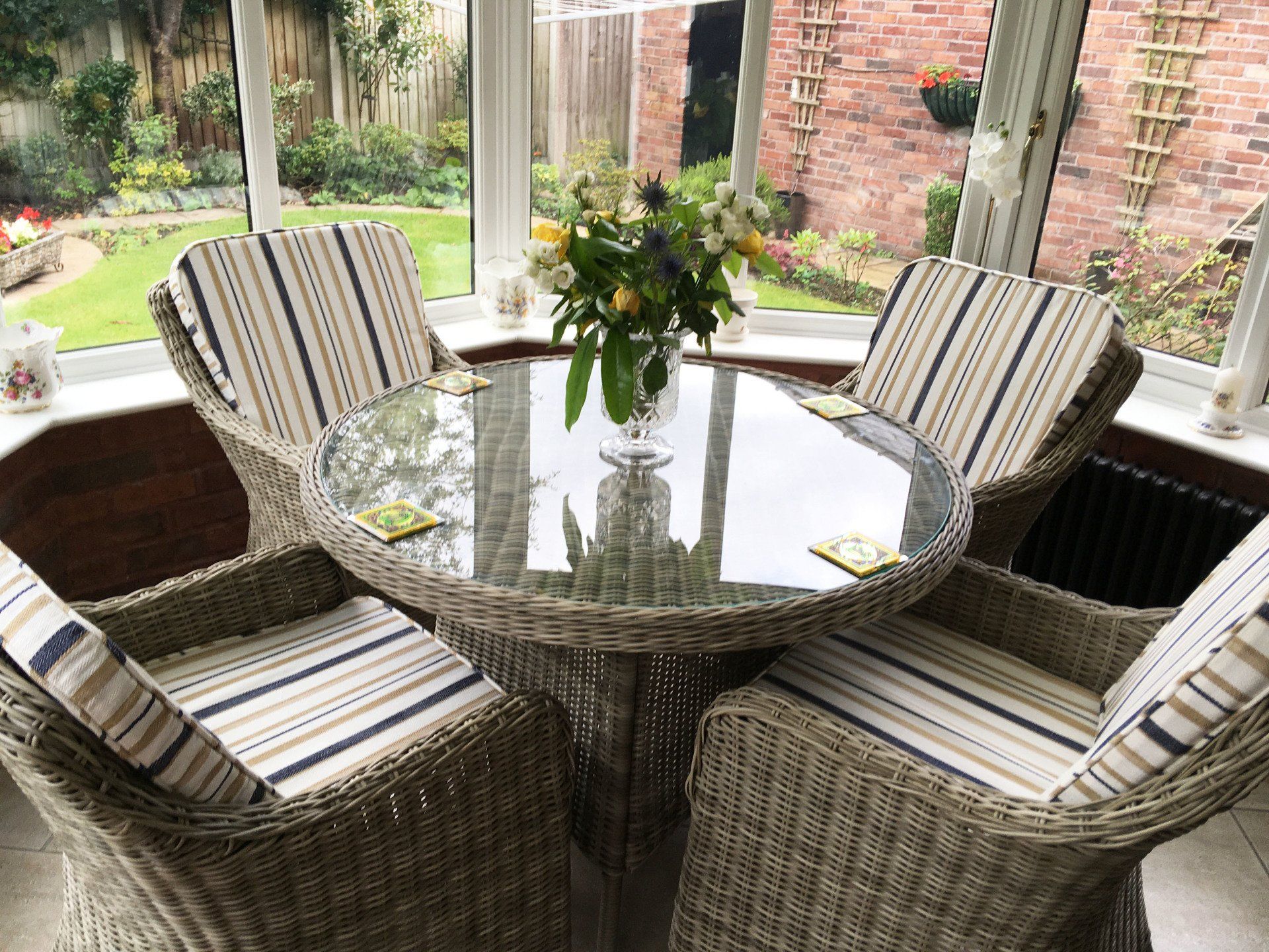 A table and chairs in a conservatory with a vase of flowers on it.