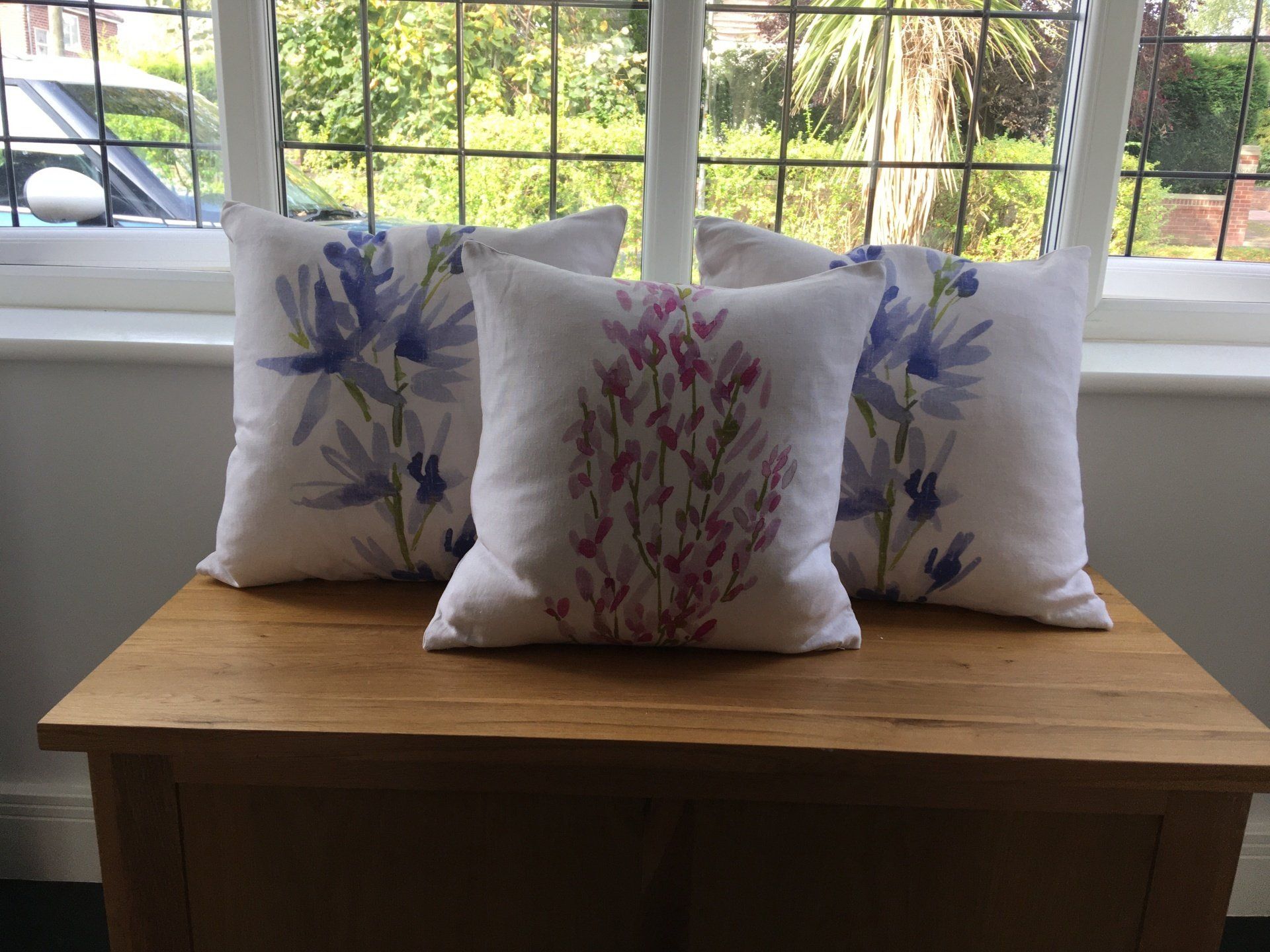 Three pillows are sitting on a wooden table in front of a window.