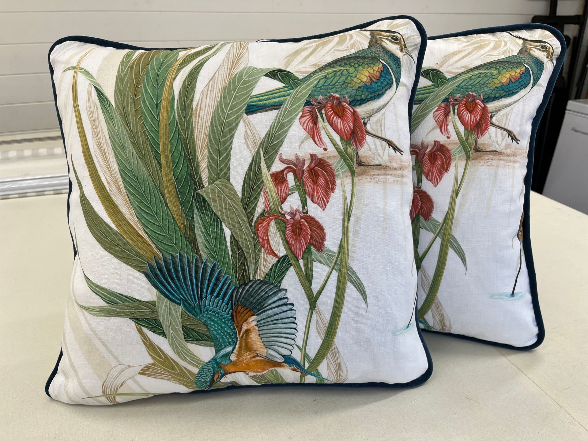 Two pillows with birds and flowers on them are sitting on a table.