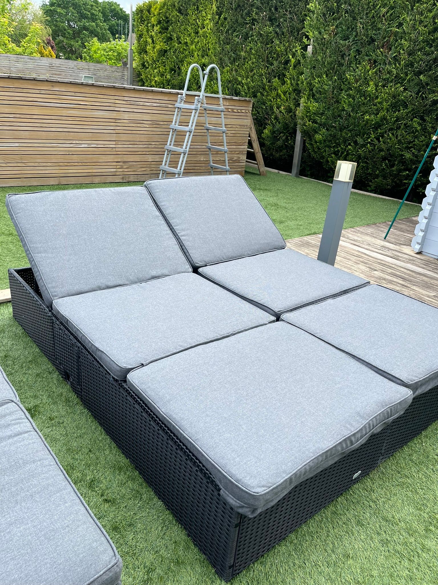 A wicker lounge chair with grey cushions is sitting on top of a lush green lawn.