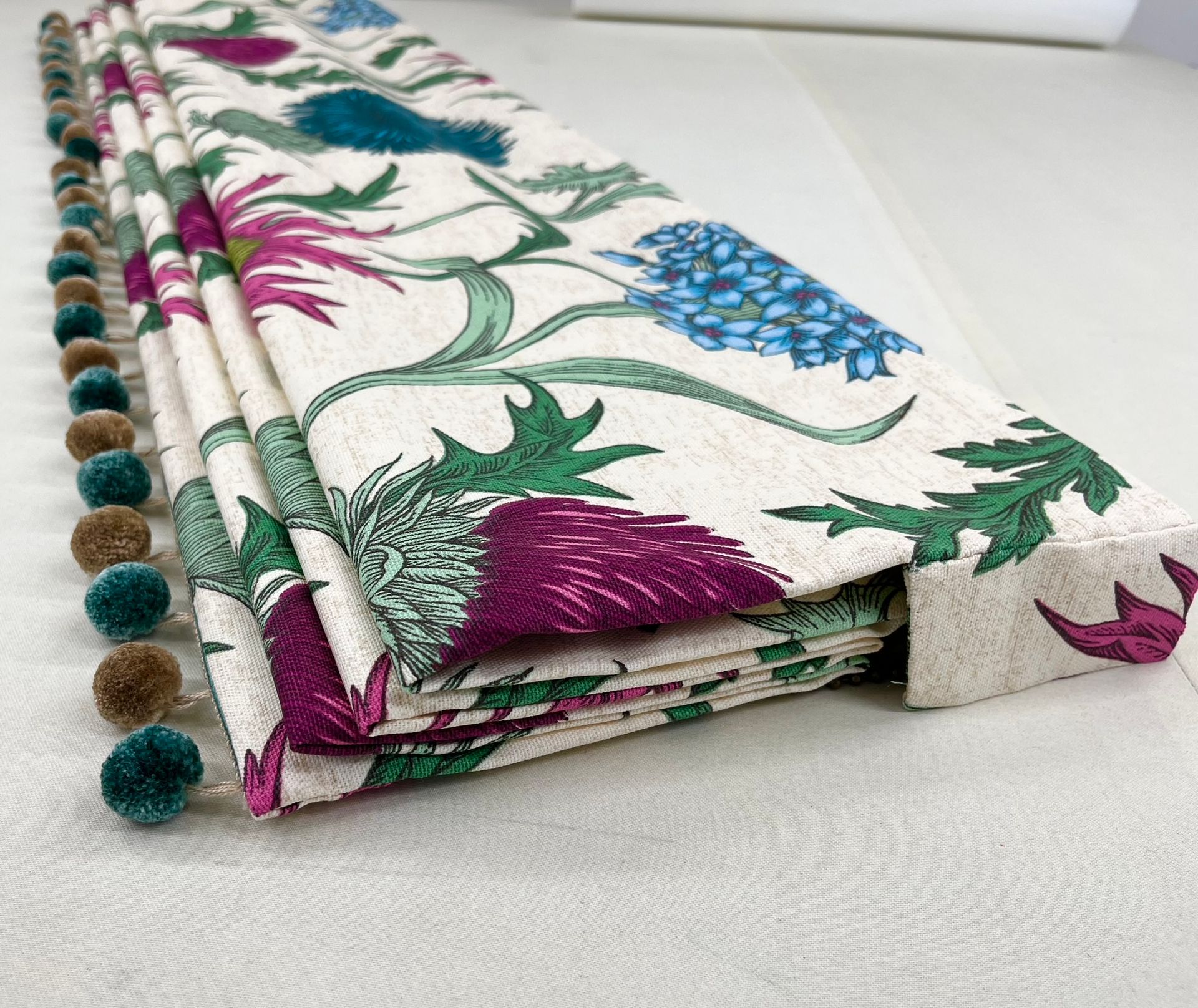 A curtain with a floral pattern and pom poms is sitting on a table.
