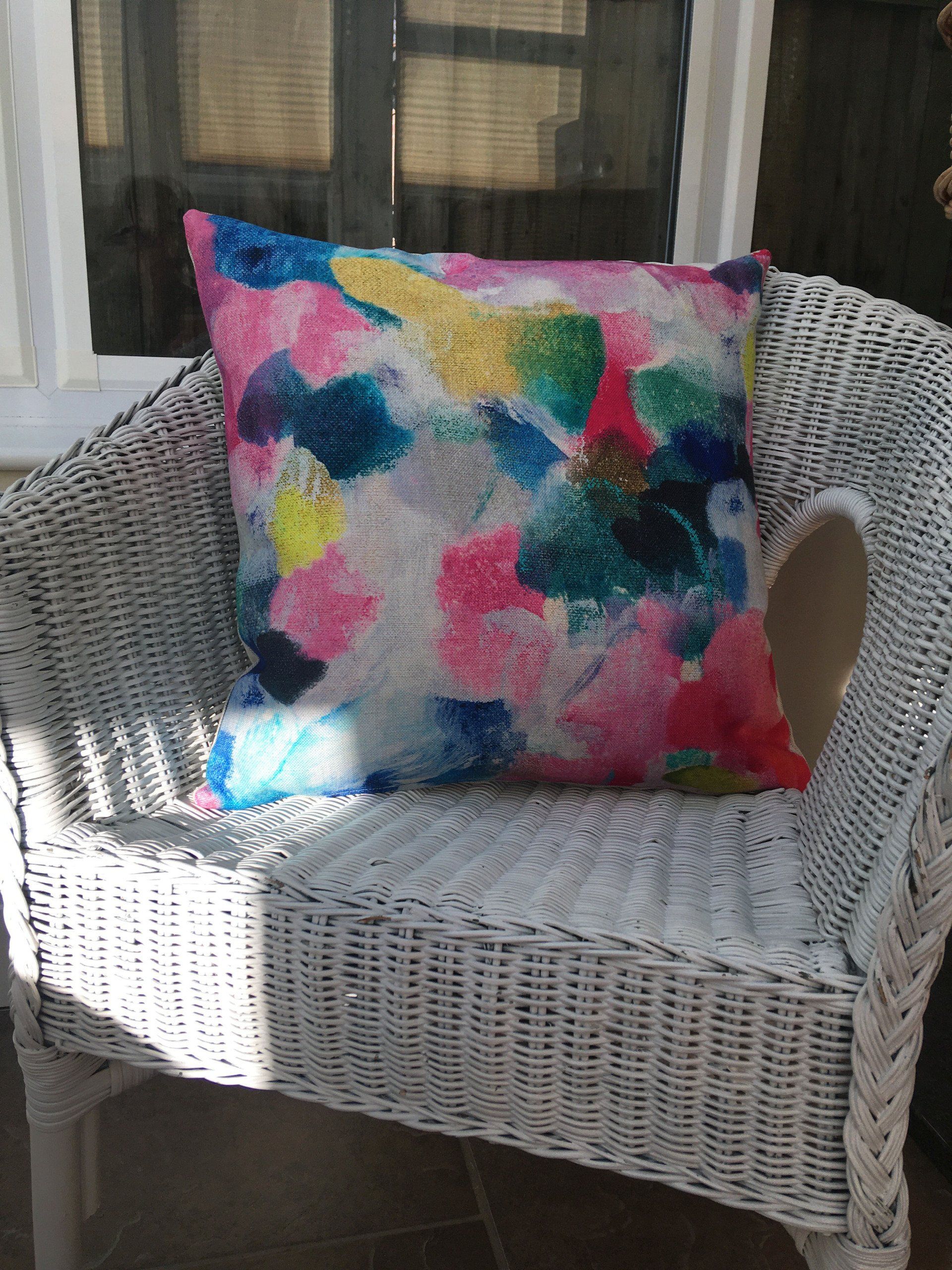A white wicker chair with a colorful pillow on it