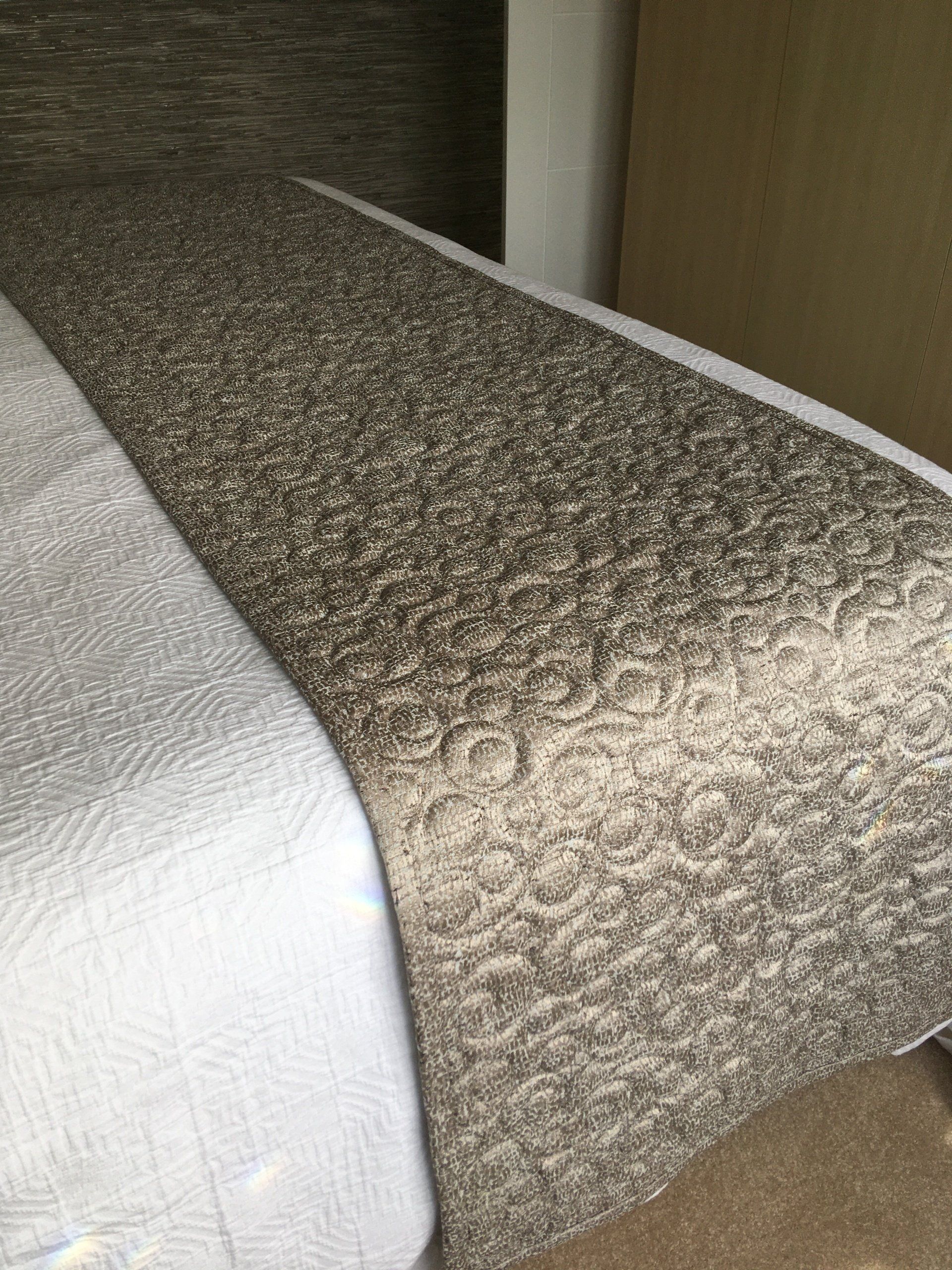 A bed with a white comforter and a brown blanket on it.