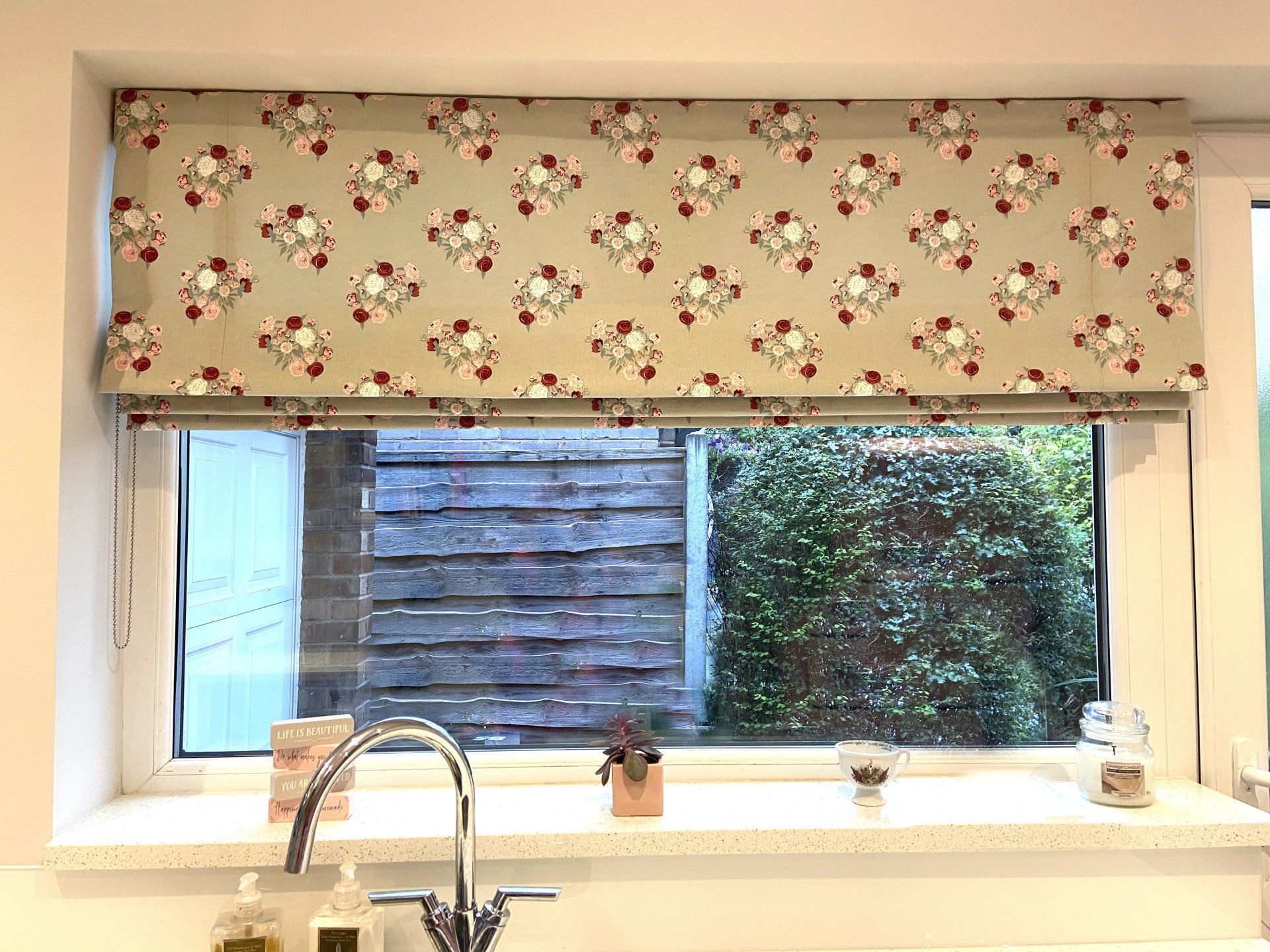 A kitchen window with a roman blind and a sink.