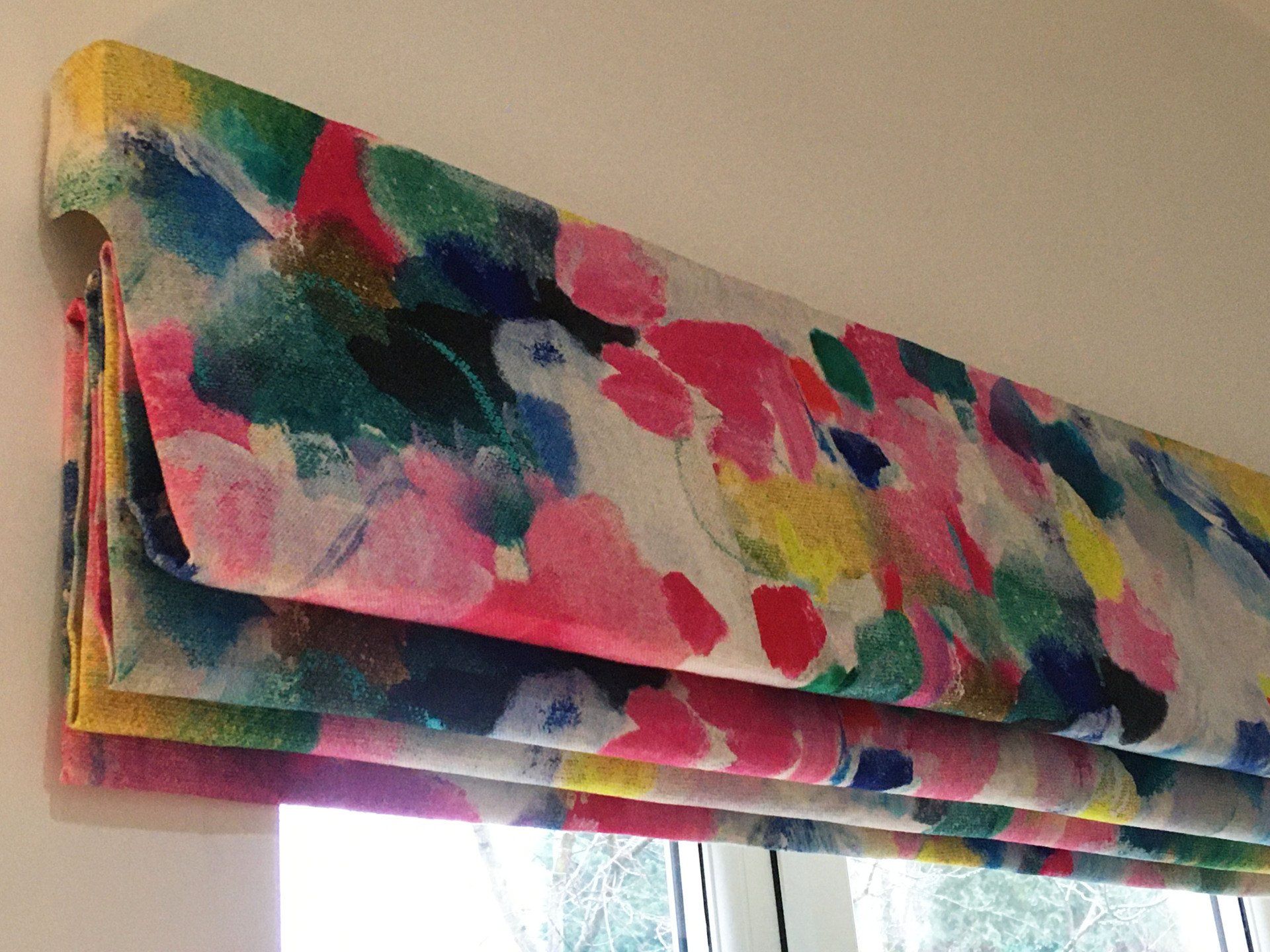 A colorful roman shade is hanging on a window.