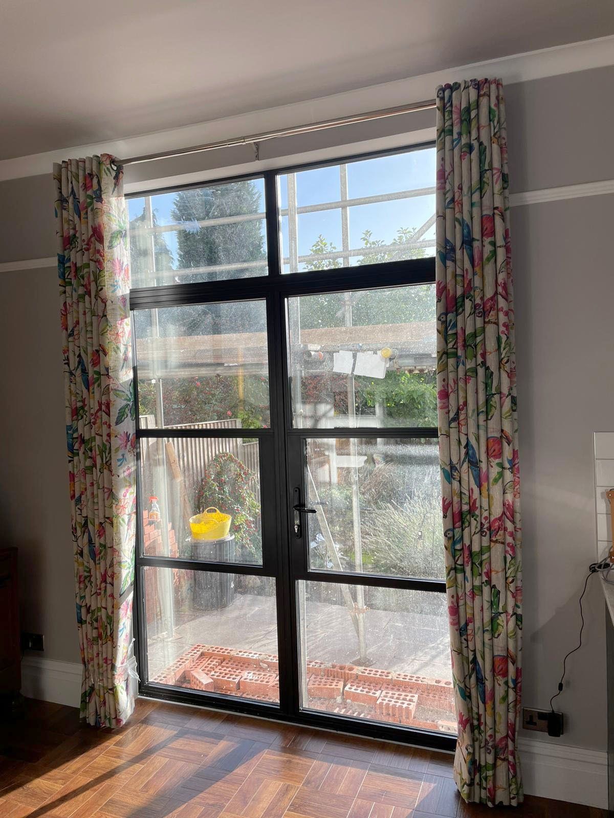 A living room with a large window and floral curtains.