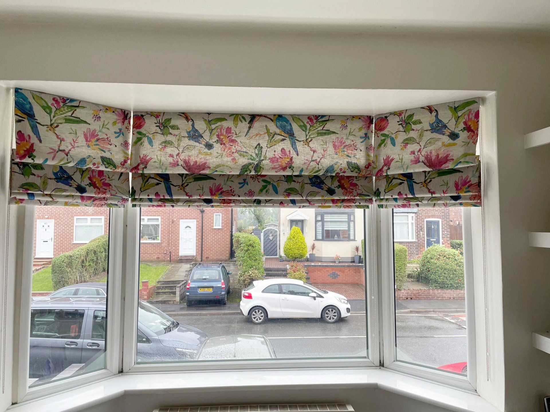 A bay window with roman blinds and a car parked in front of it.