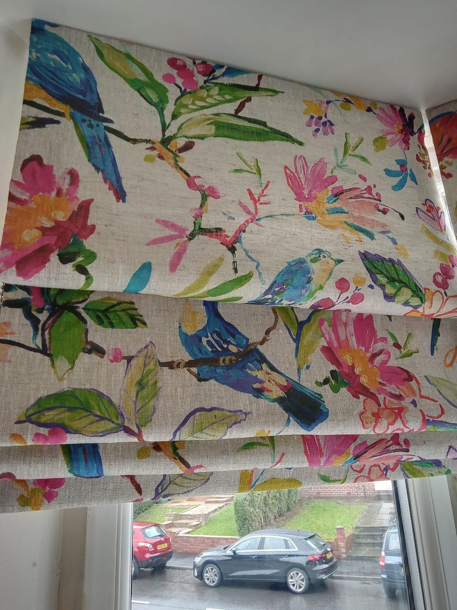 A window with a colorful roman shade with birds and flowers on it.