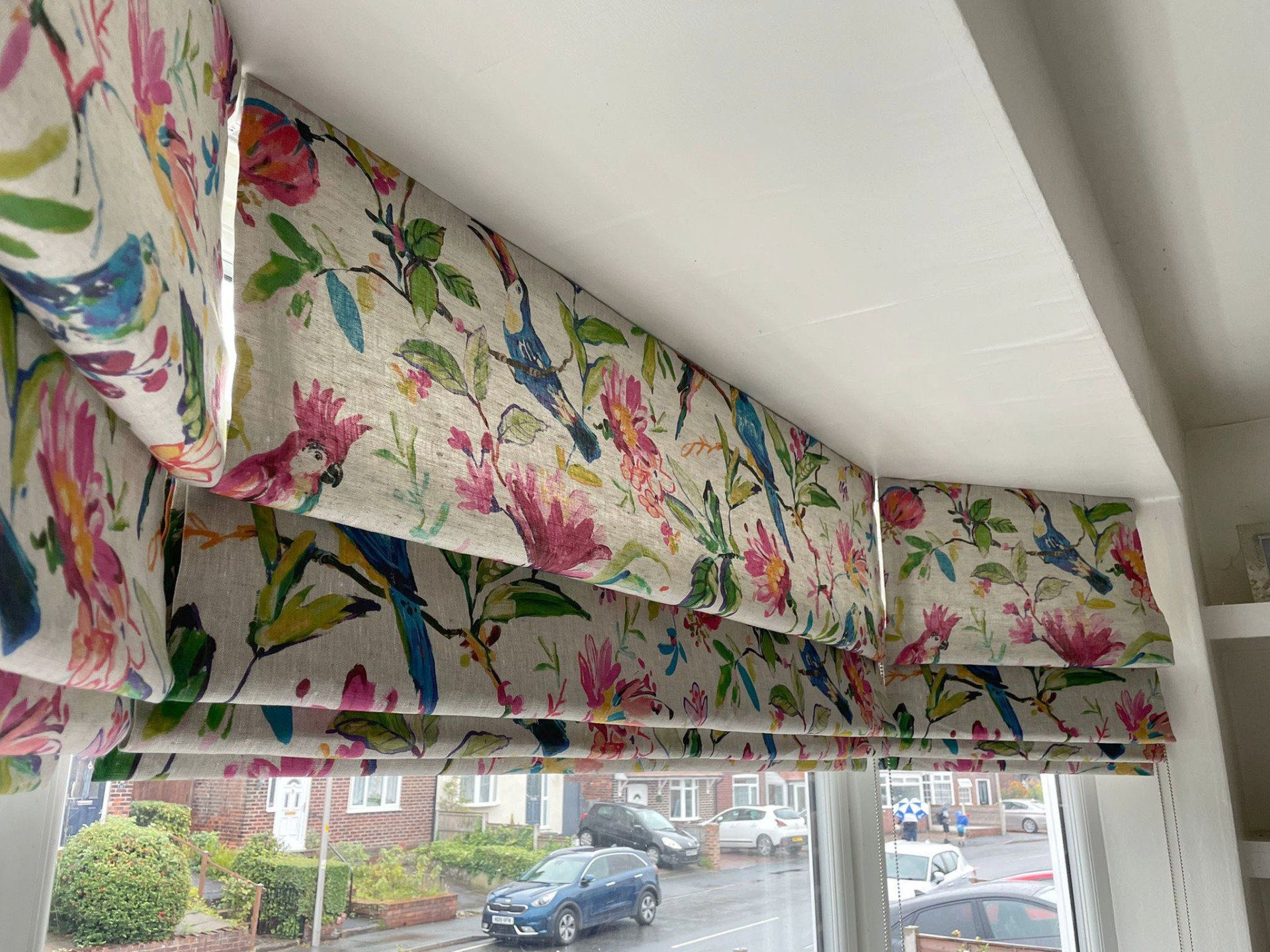 A window with a floral pattern on the blinds and a view of a street.