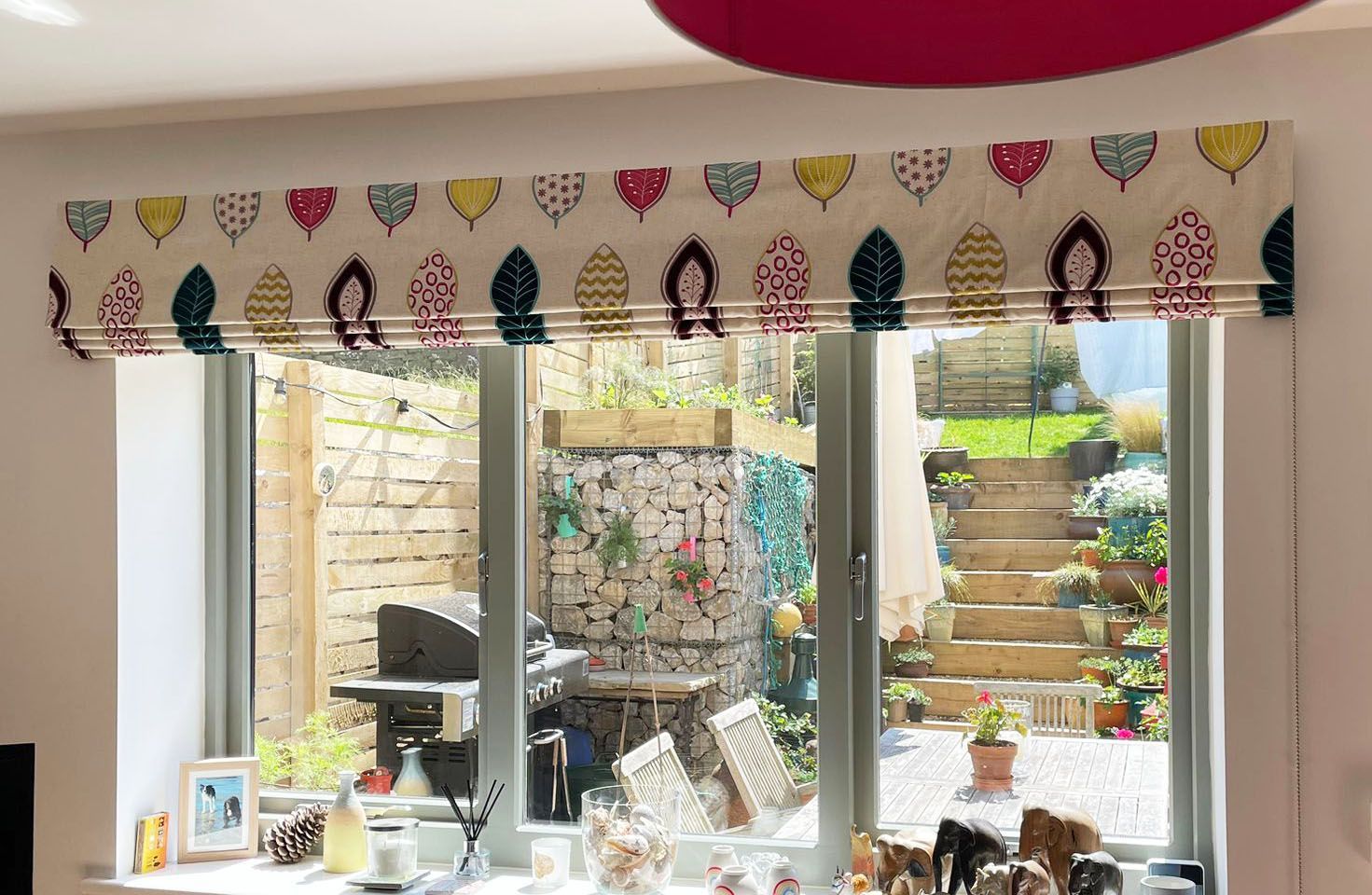 A window with a colorful blind on it and a view of a garden.