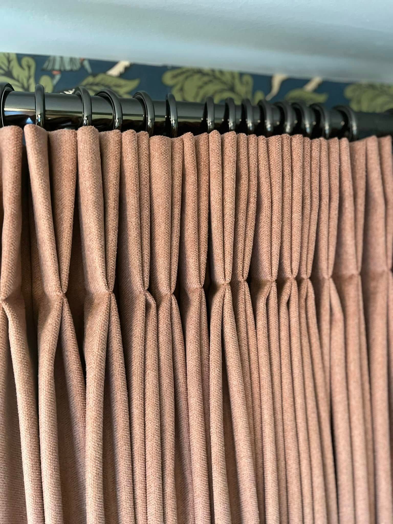 A close up of a pair of pink curtains hanging on a curtain rod.