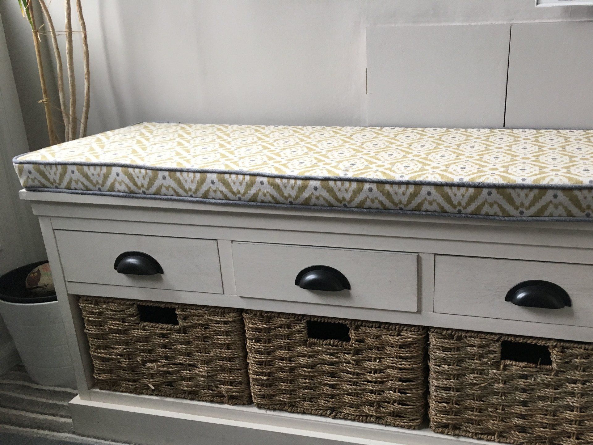 A white bench with wicker baskets and drawers underneath it.