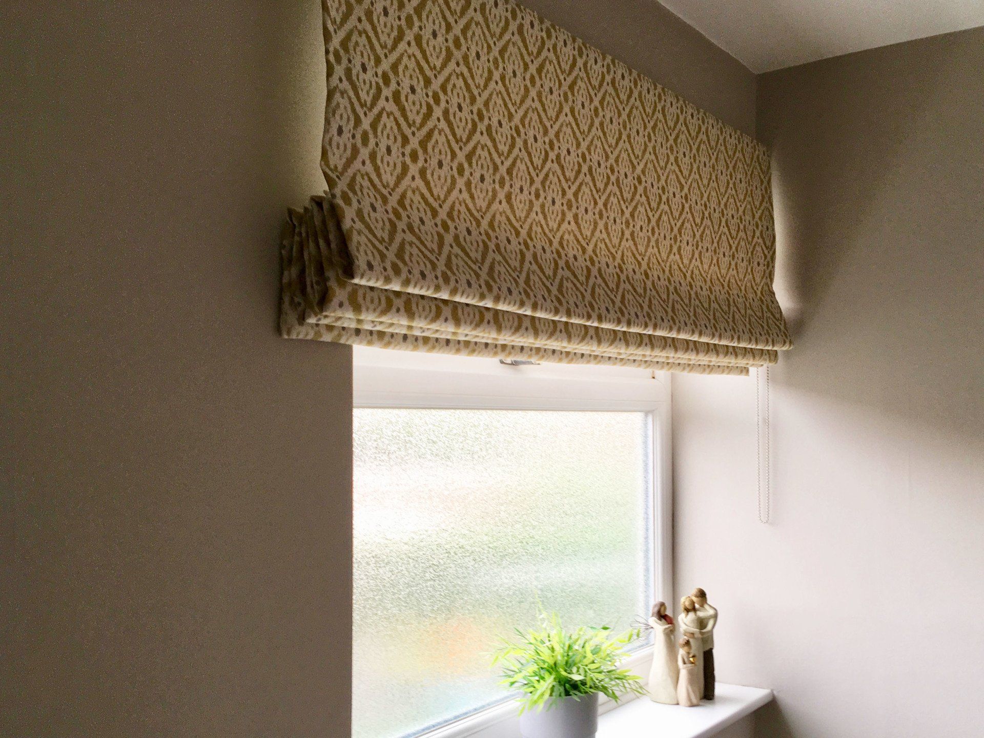 A window with a roman blind on it and a potted plant on a window sill.