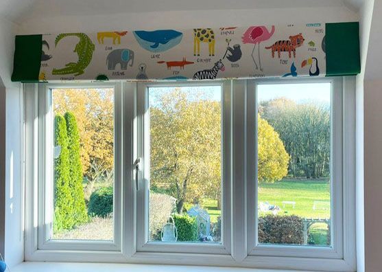A window with a curtains with animals on it and a view of a field.