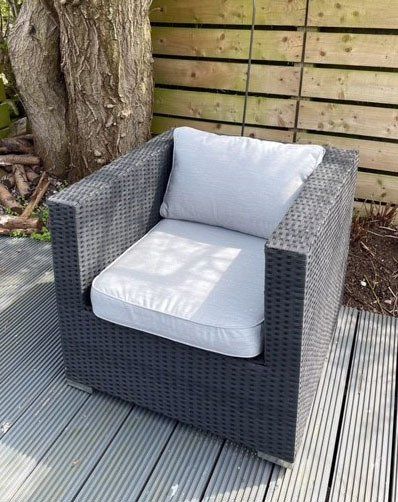 A wicker chair with a white cushion is sitting on a wooden deck.