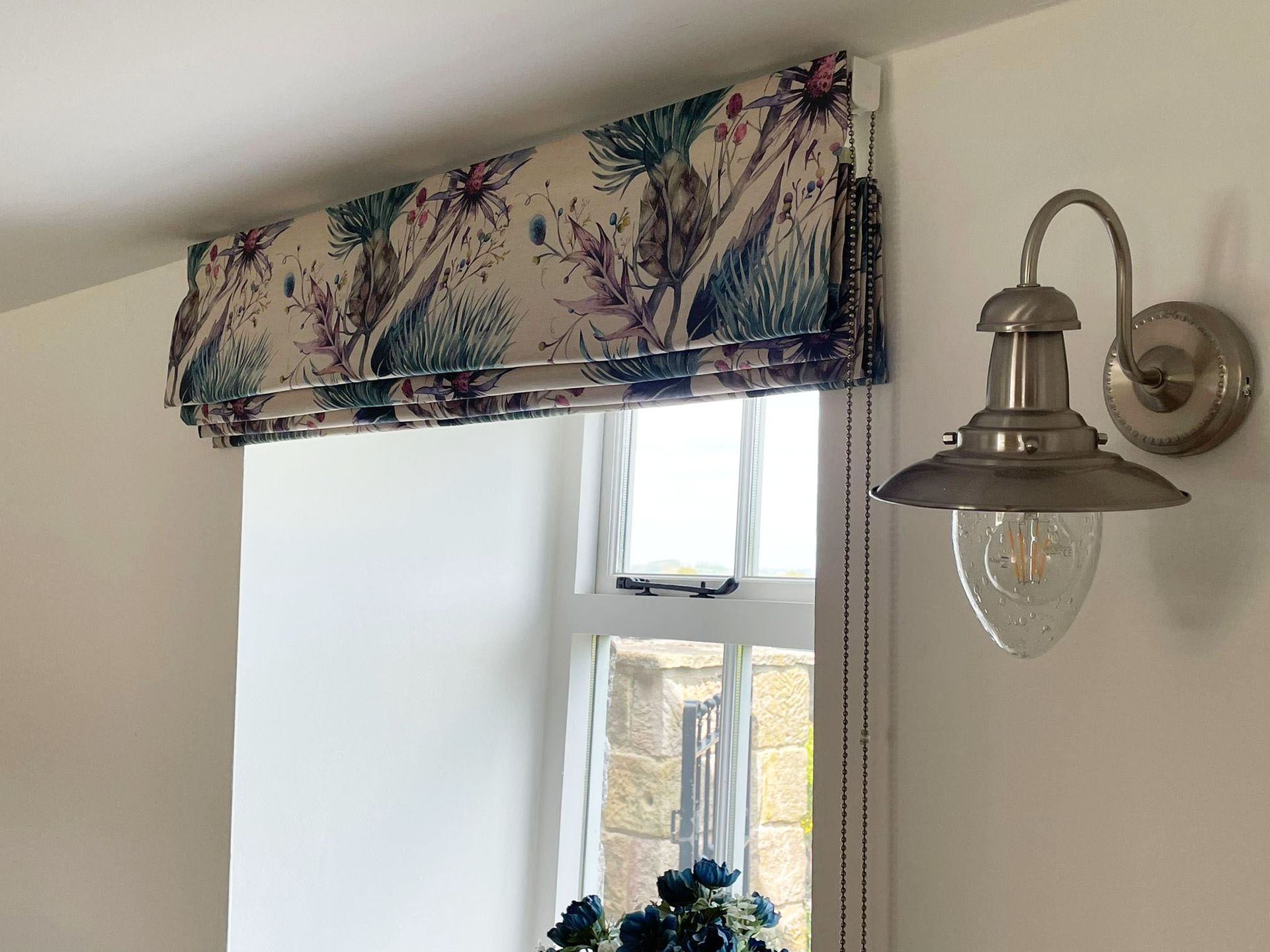 A window with a roman blind and a light on the wall.