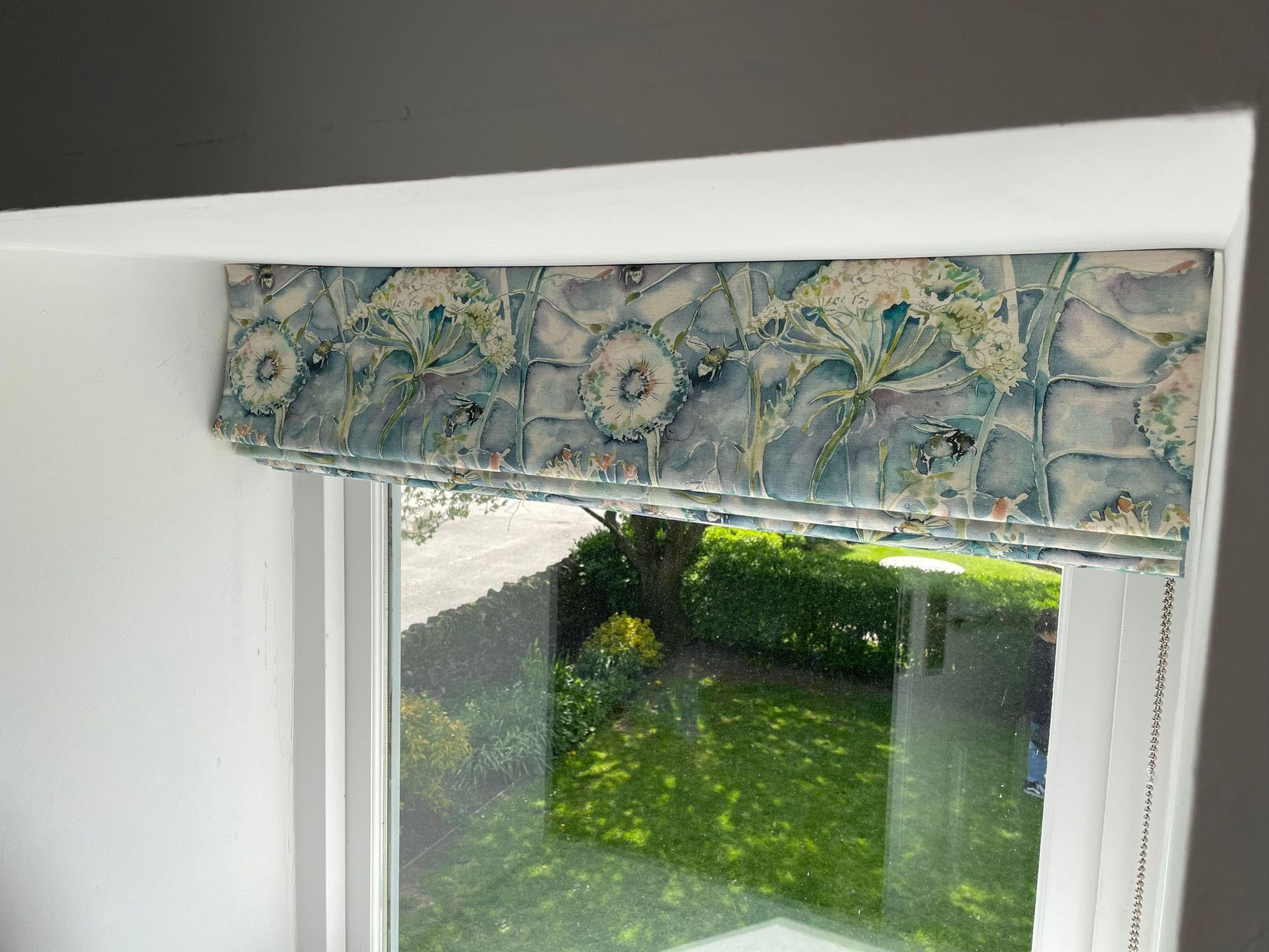 A window with a roman shade on it and a view of a garden.