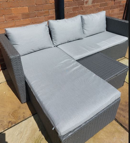 A wicker sectional couch with grey cushions and pillows