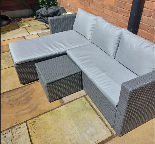 A wicker sectional couch with grey cushions sits on a patio