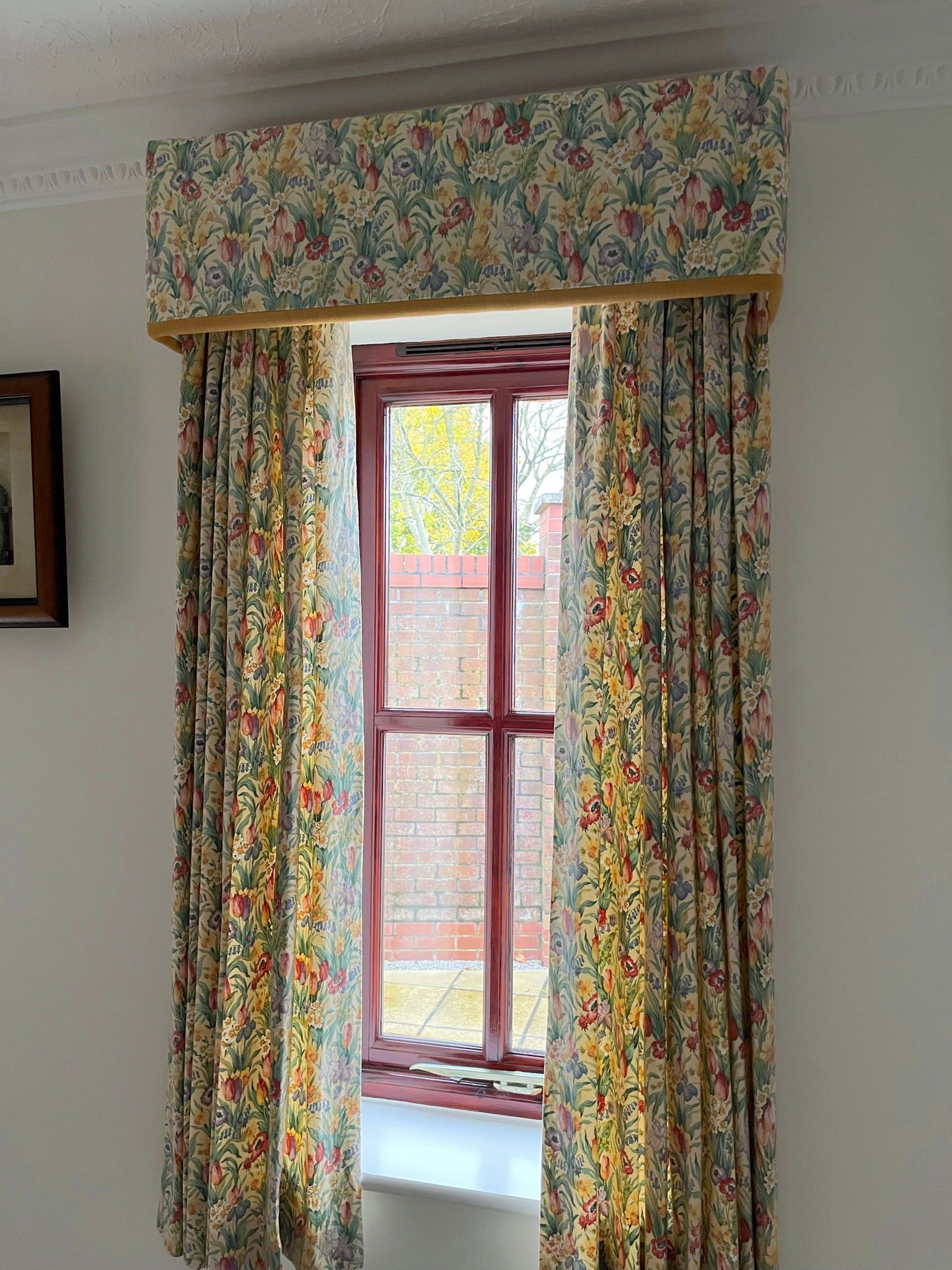 A window with floral curtains and a picture on the wall.