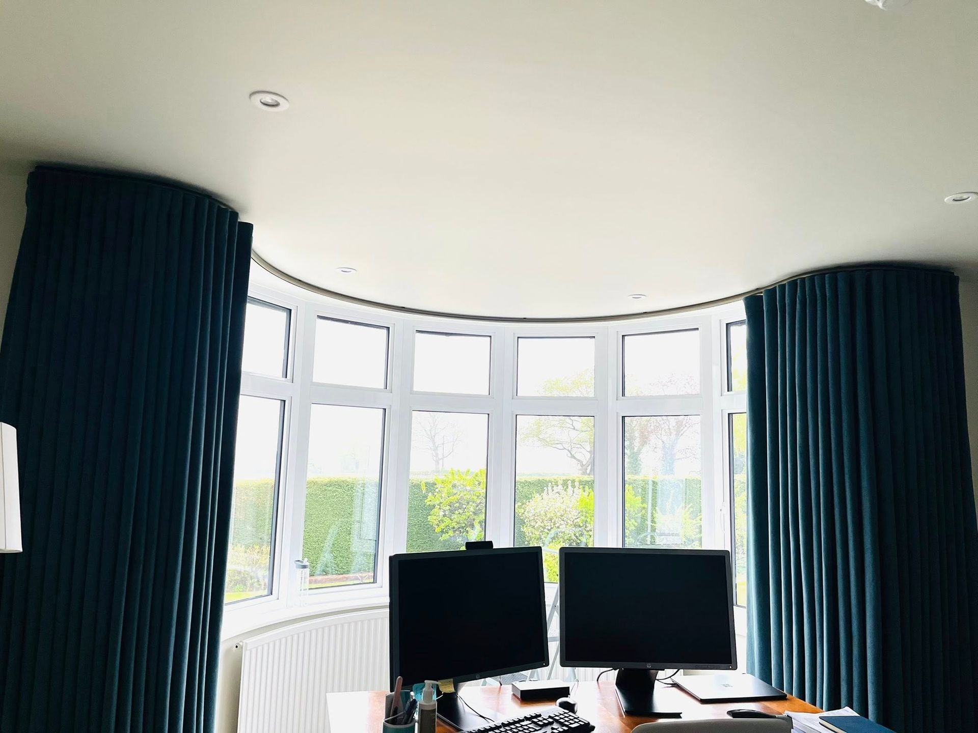 Two computer monitors are sitting on a desk in front of a large window.