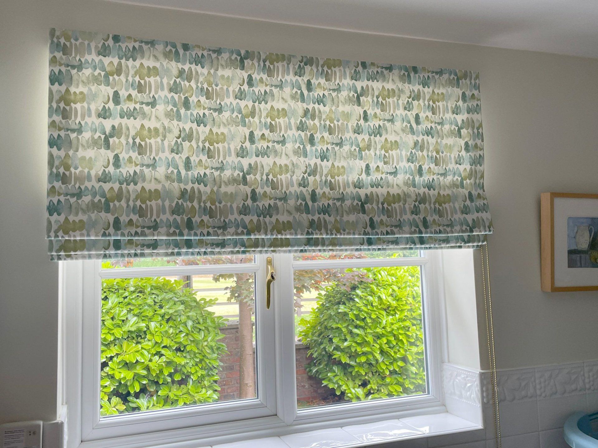 A window with a roman blind on it and a picture on the wall.