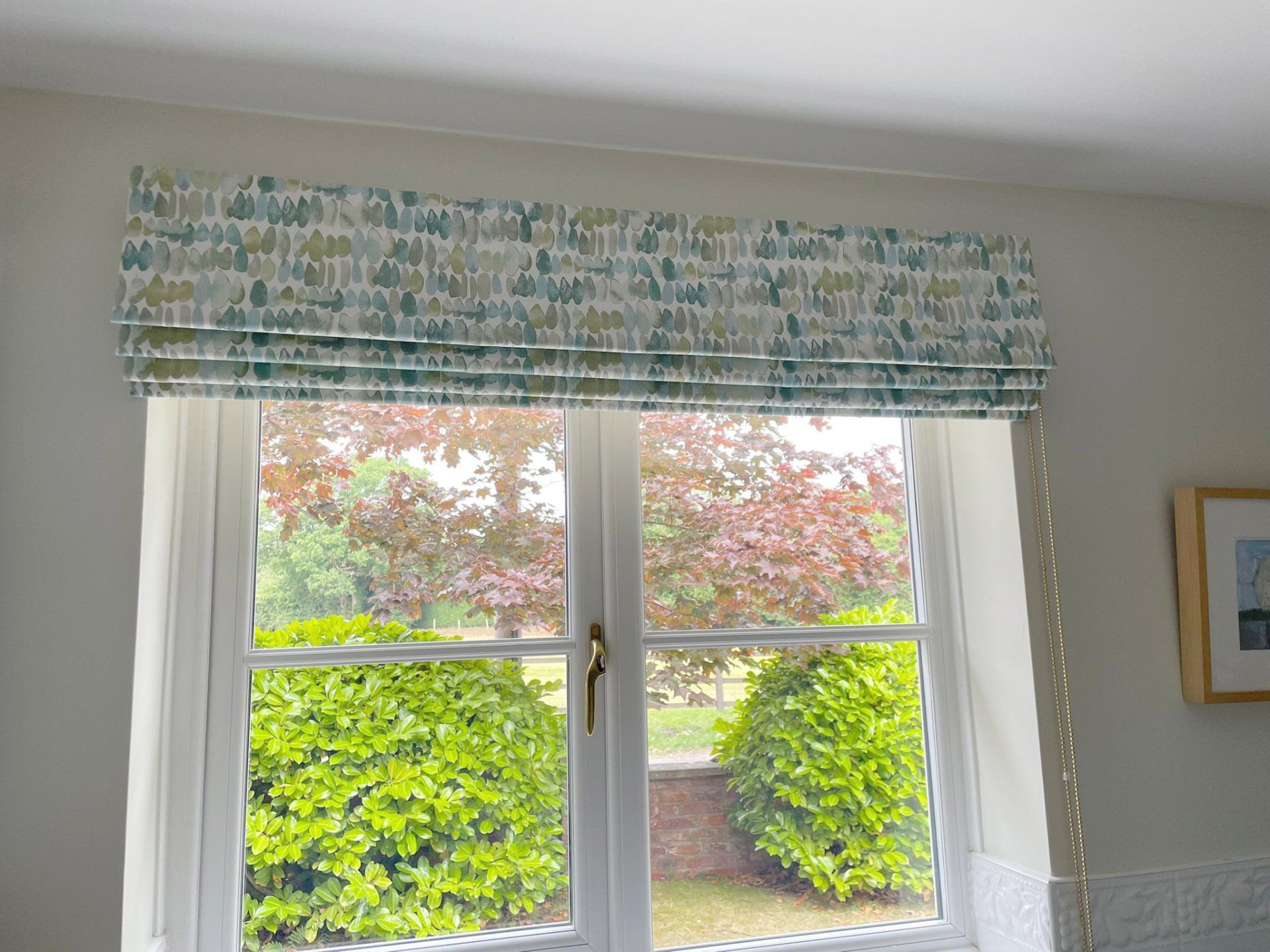 A window with a roman shade on it and a picture on the wall.