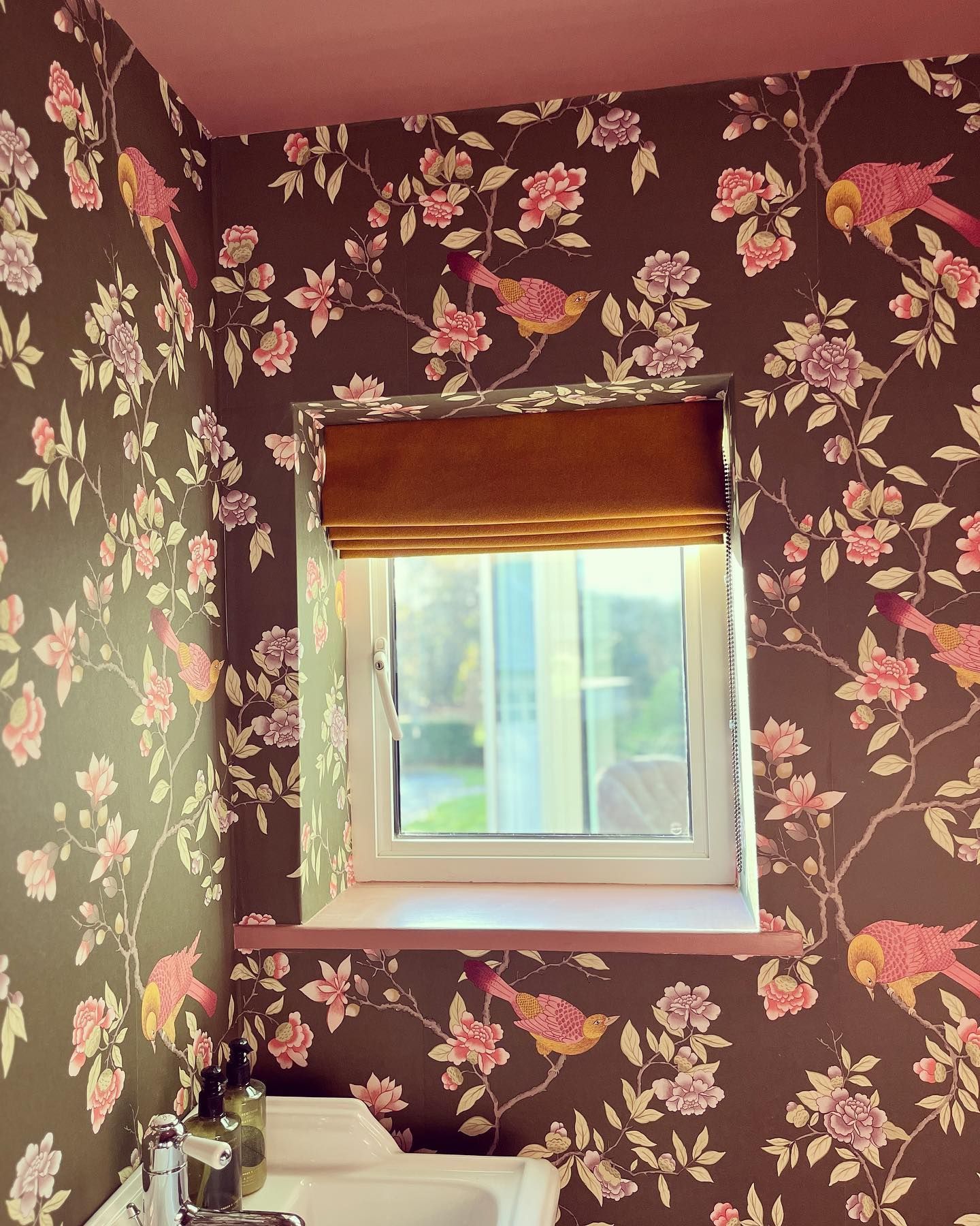 A bathroom with a sink and a window with a floral wallpaper