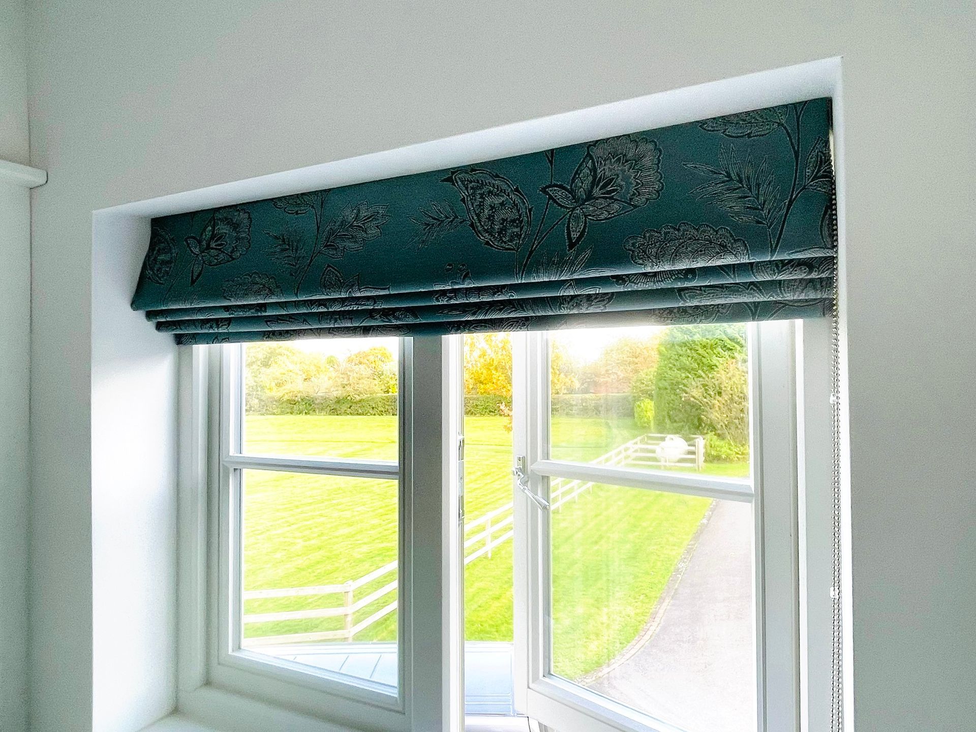 A window with a blue blind on it and a view of a field.