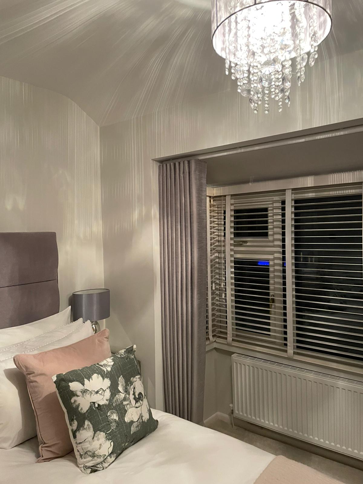 A bedroom with a bed , window , lamp and chandelier.