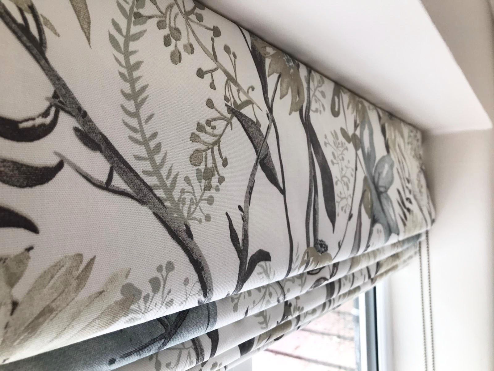 A window with a roman shade with a floral pattern on it.