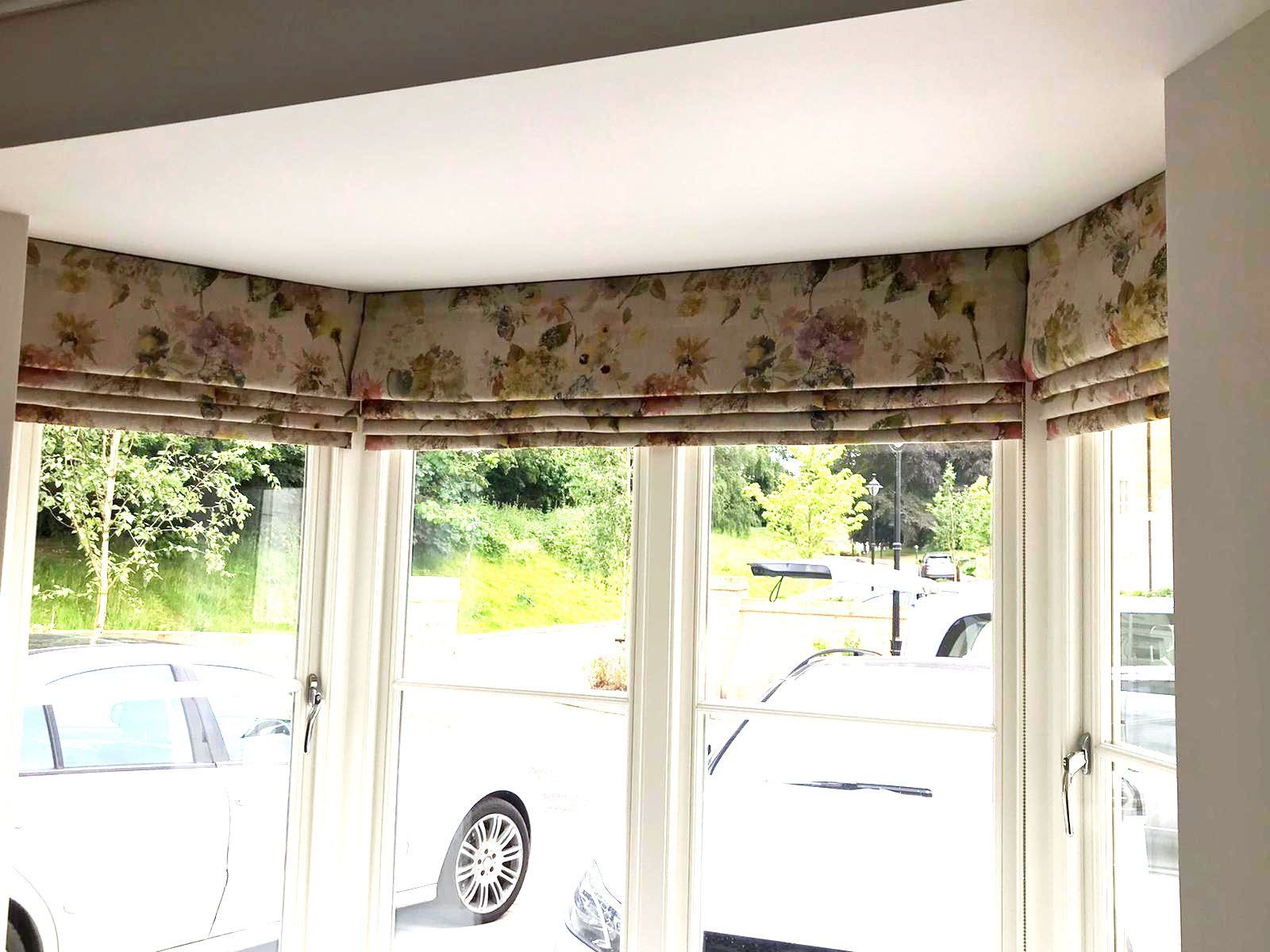 A living room with a bay window and roman blinds.