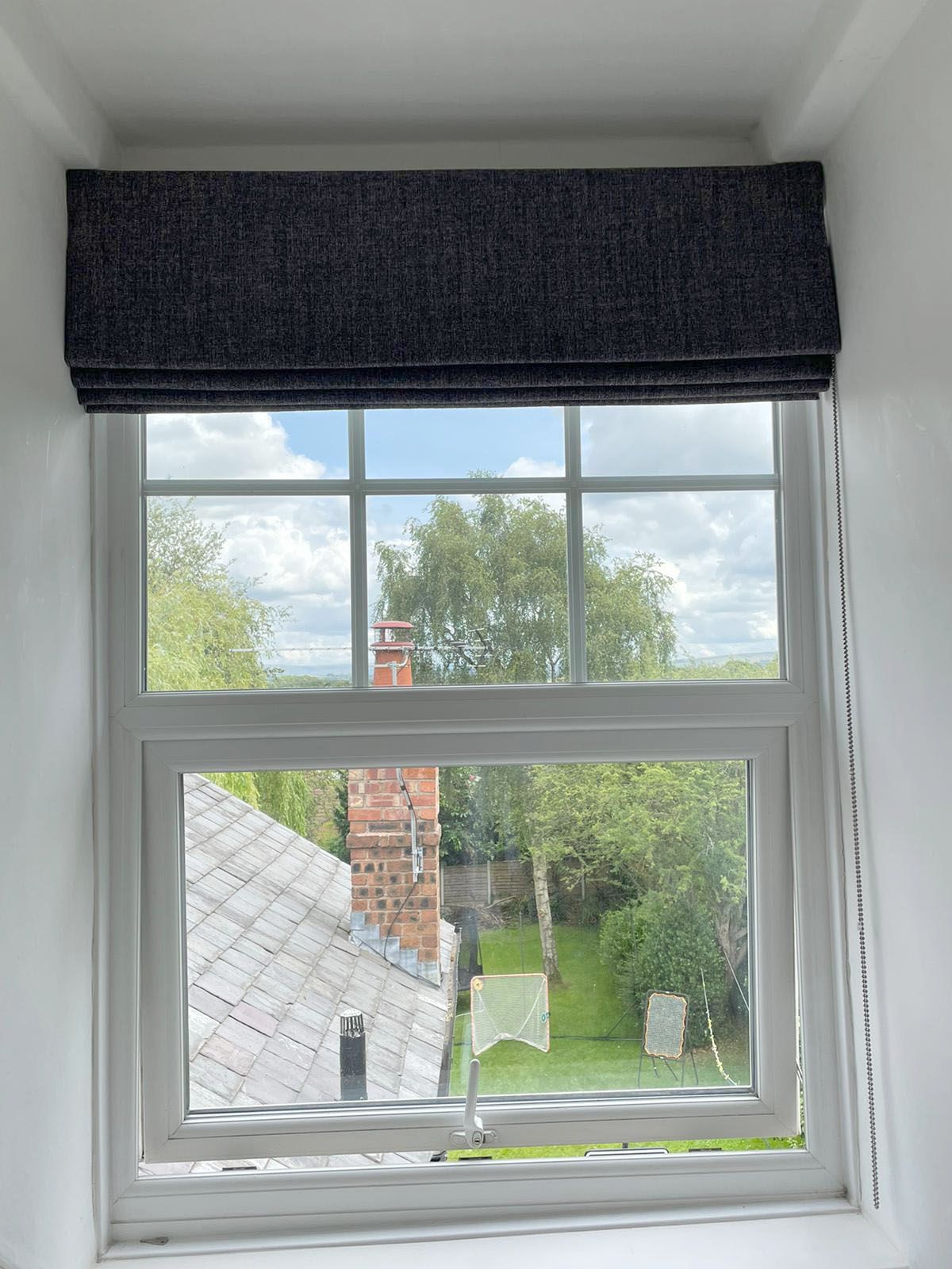 A window with a black blind on it and a view of a garden.