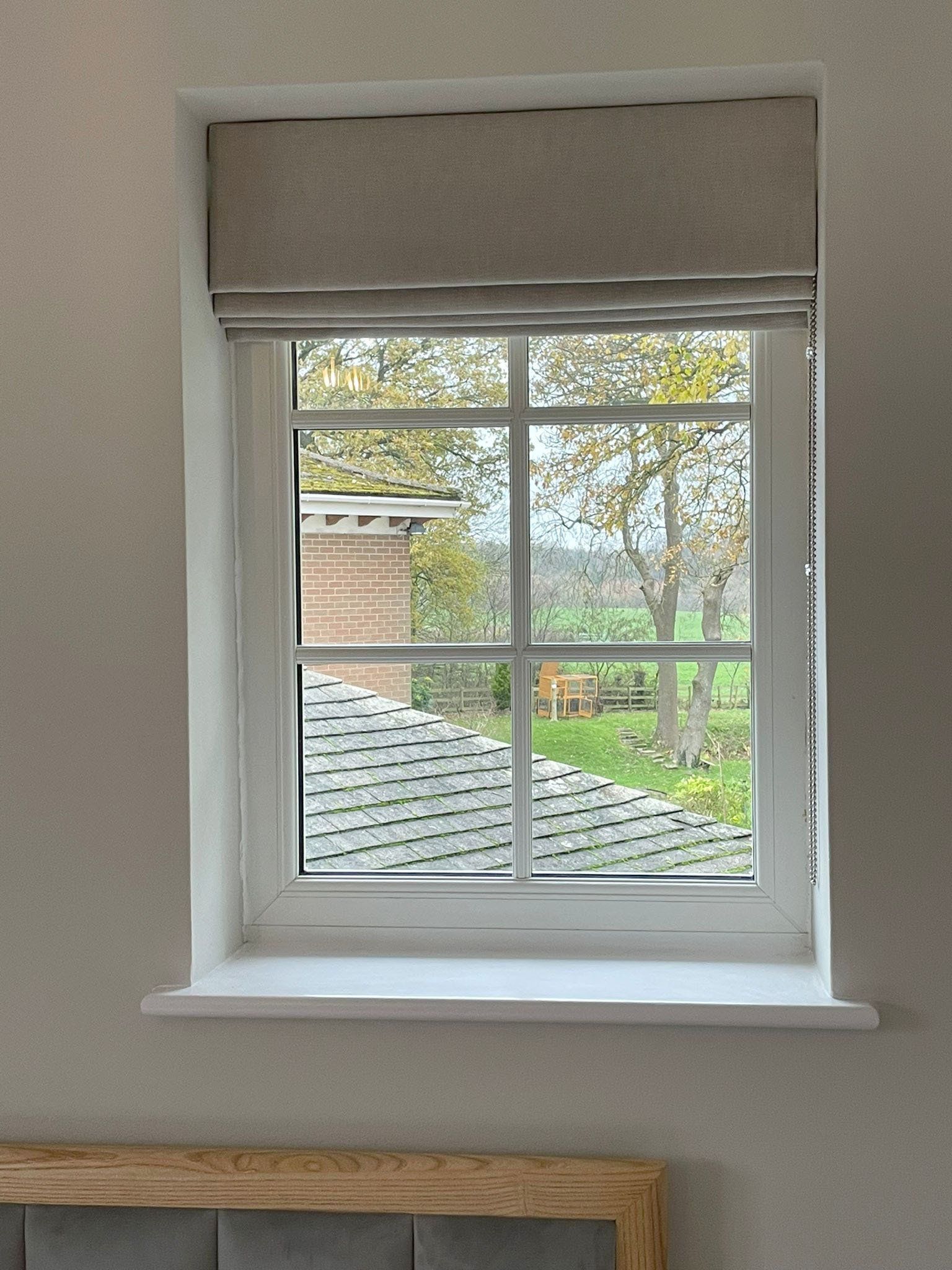 A bedroom window with a view of a roof and trees.