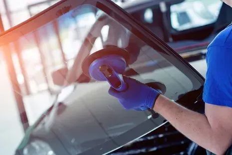 Person in blue gloves using a suction cup tool to remove a windshield from a car.