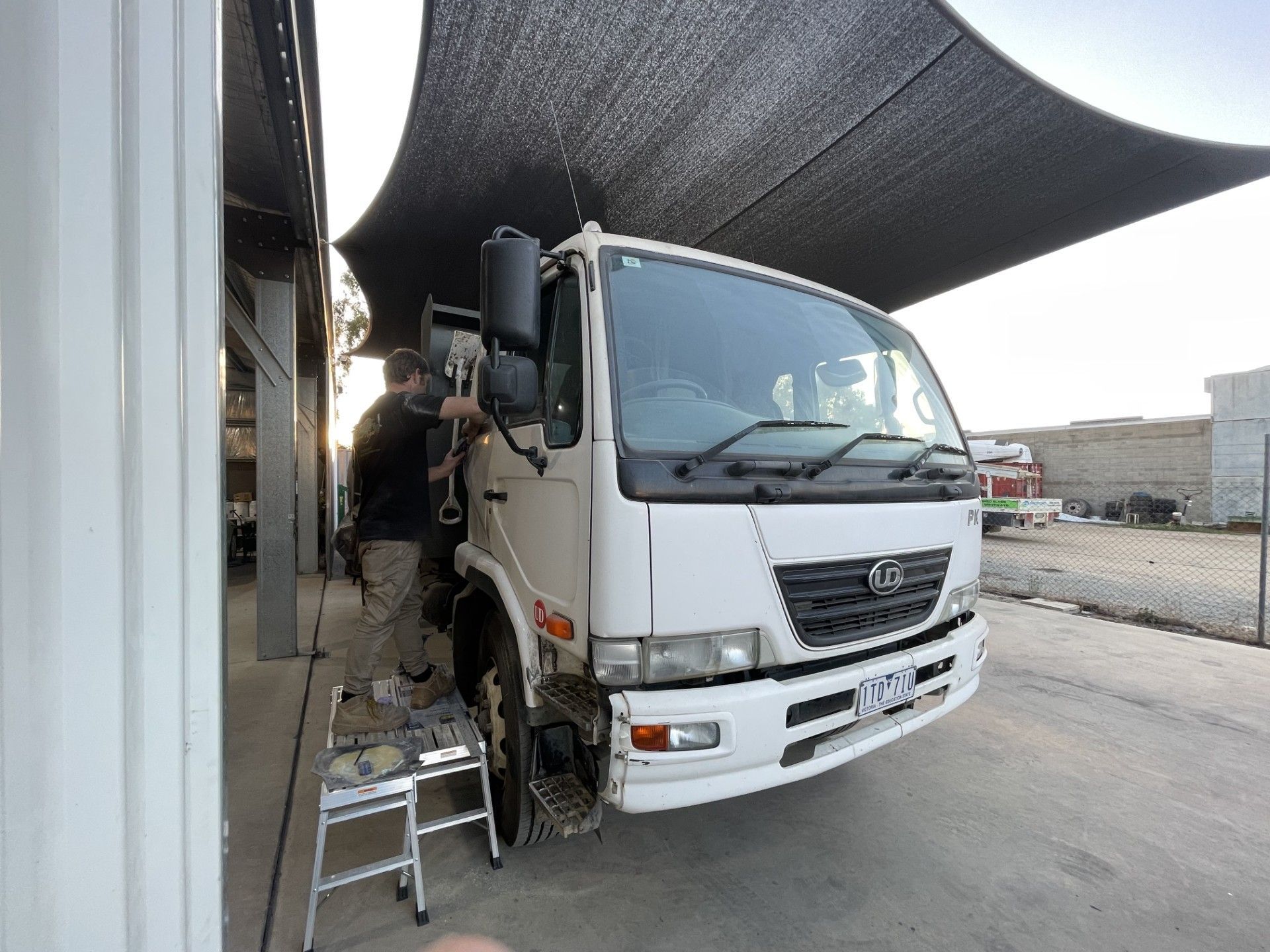 A man working on a white truck parked under a black shade in an outdoor setting — Panel Pro Smash Repairs in Wodonga, VIC
