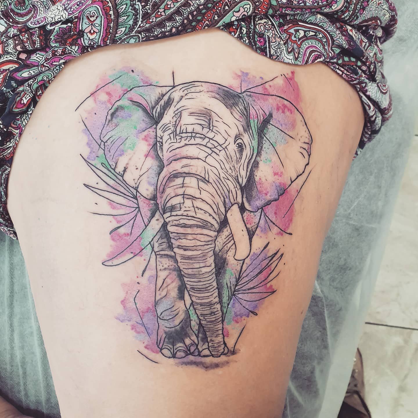 Elephant tattoo on thigh, with watercolor splashes of purple and green.