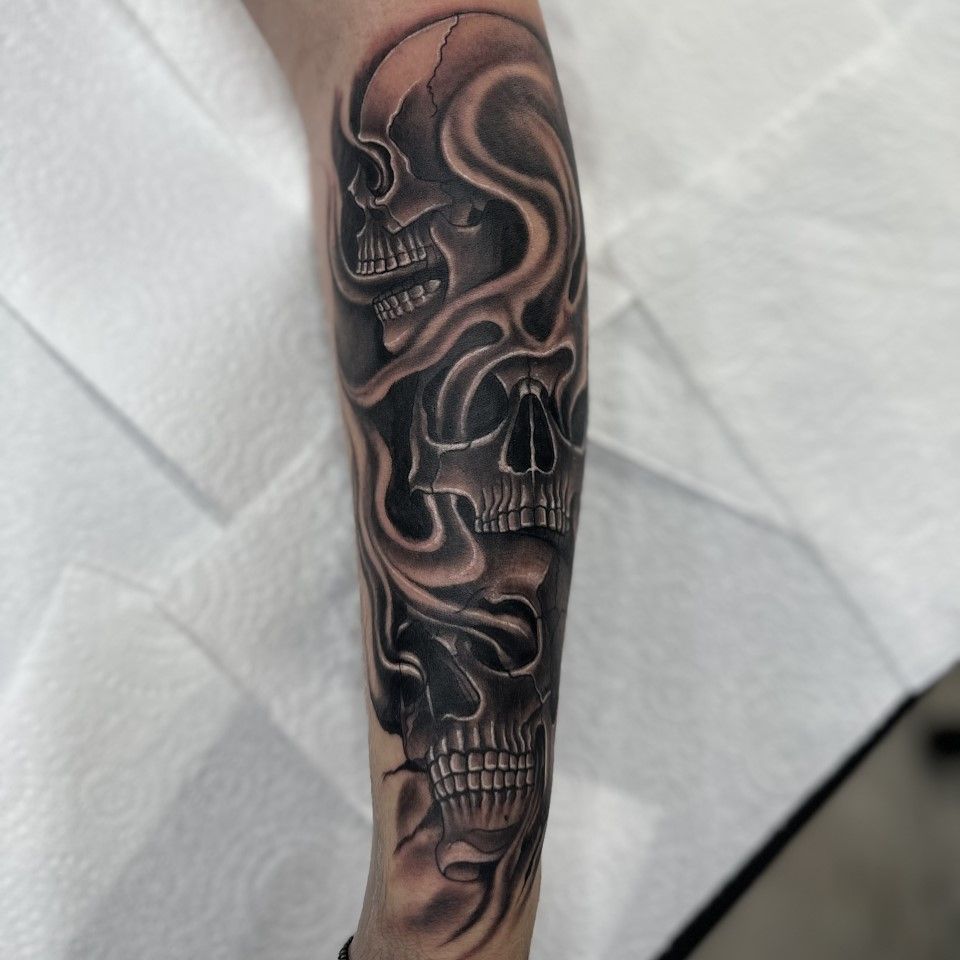 Tattoo of three stylized skulls, with smoky effects, on a forearm in black and gray ink. — Whitsunday Tattooing Airlie Beach in Whitsundays, QLD