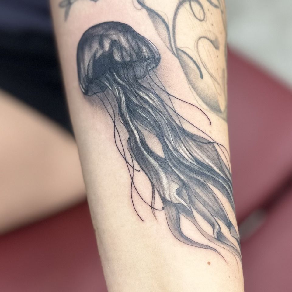 Tattoo of a black jellyfish on a person's arm, with long flowing tentacles. — Whitsunday Tattooing Airlie Beach in Whitsundays, QLD