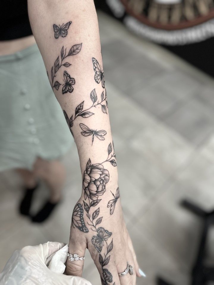 Tattoo of butterflies, flowers, and vines on an arm, with a gloved hand holding the arm.