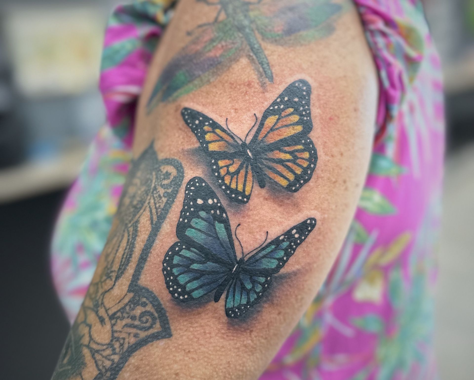 Tattoo of two butterflies, one orange and black, one teal and black, on a person's arm. — Whitsunday Tattooing Airlie Beach in Whitsundays, QLD