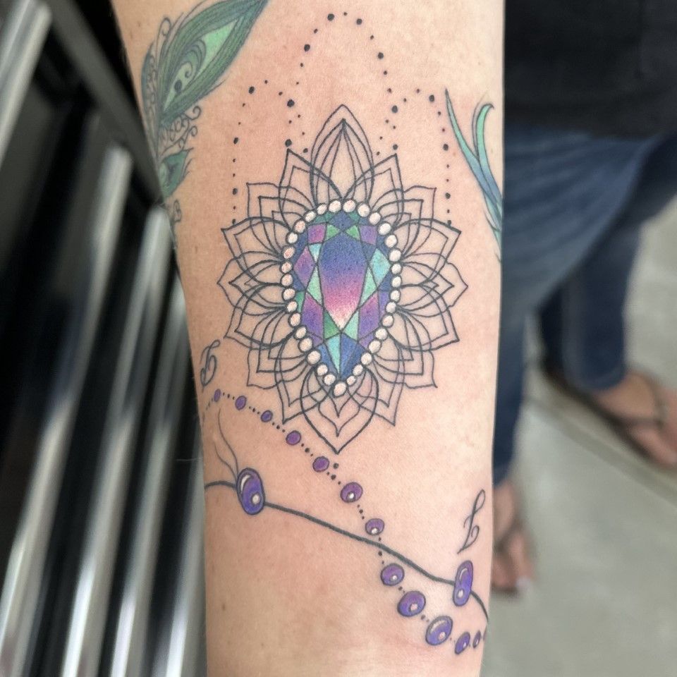 Tattoo of a teardrop-shaped gemstone in shades of blue, purple, and green, surrounded by a floral design and dotted line. — Whitsunday Tattooing Airlie Beach in Whitsundays, QLD