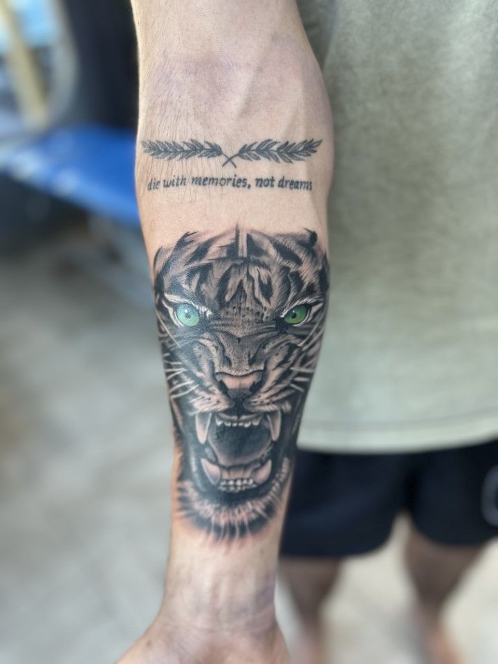 Arm tattoo featuring a roaring tiger with green eyes, text