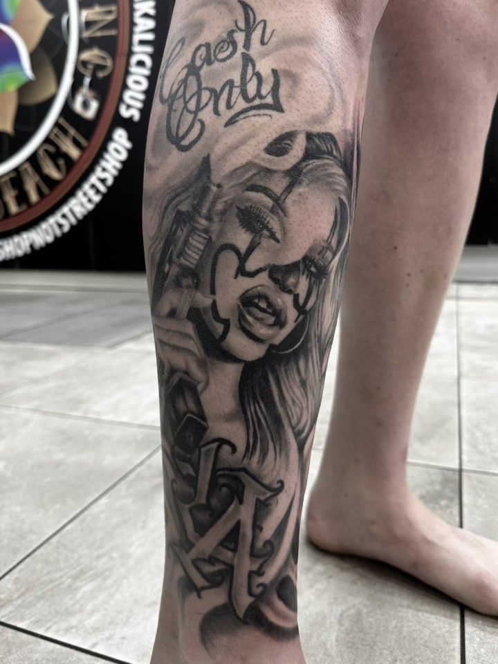 Tattoo on a leg featuring a woman with clown makeup holding a gun, text