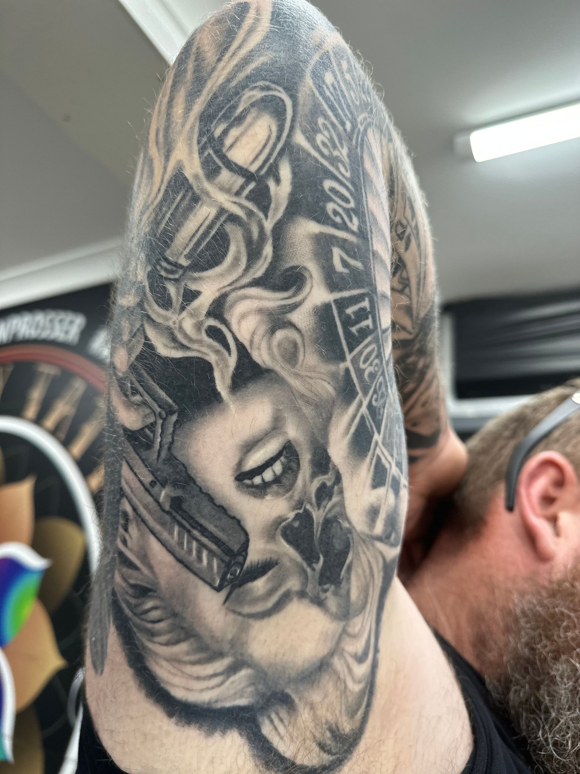 Tattoo on upper arm featuring a woman's face, guns, smoke, and roulette numbers. Monochrome. — Whitsunday Tattooing Airlie Beach in Whitsundays, QLD